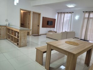 A modern living room with a wooden dining table, a sofa, and a TV mounted on the wall. - Pata la Gaullette (La Gaulette)