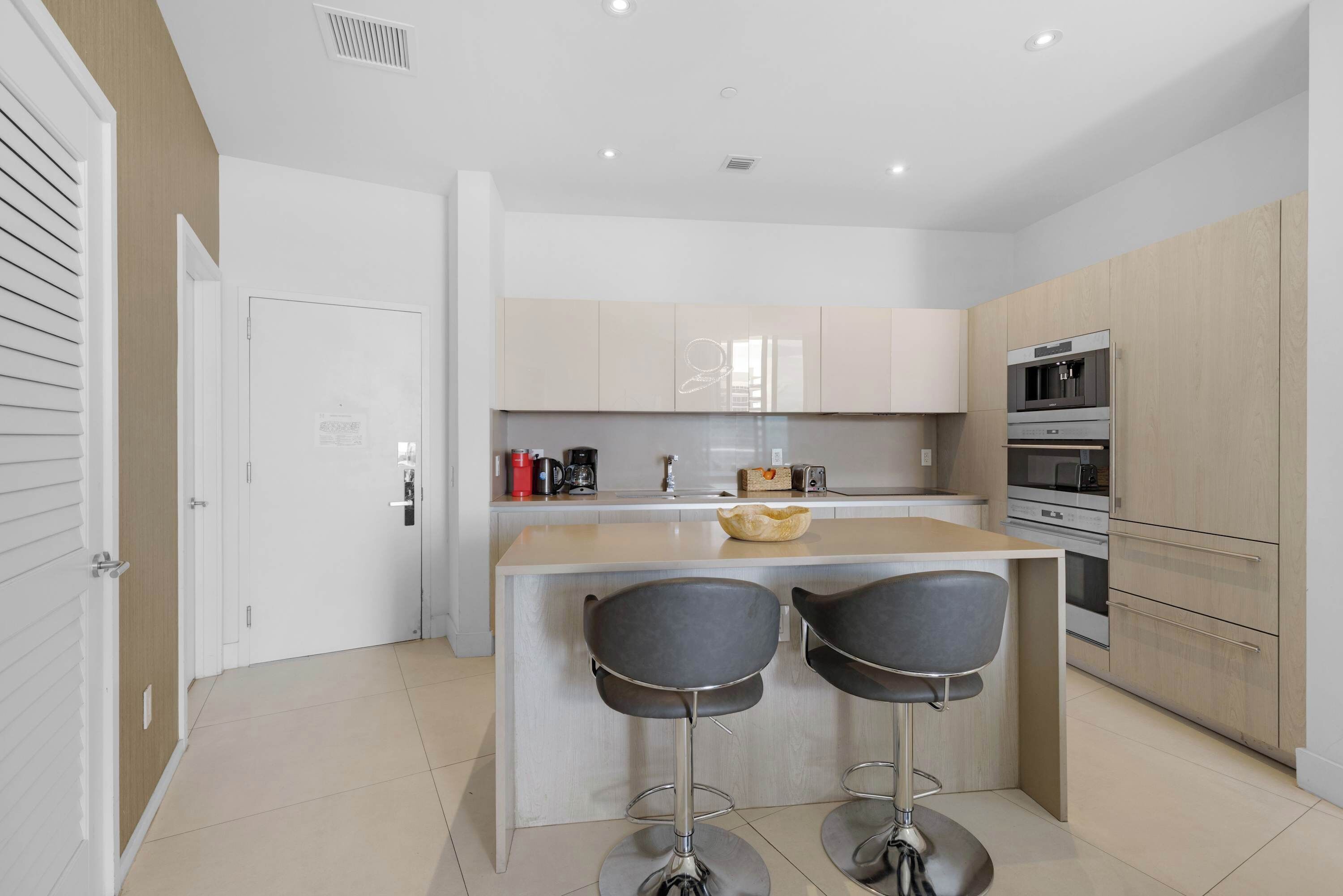 A modern kitchen with a central island, two bar stools, and built-in appliances.