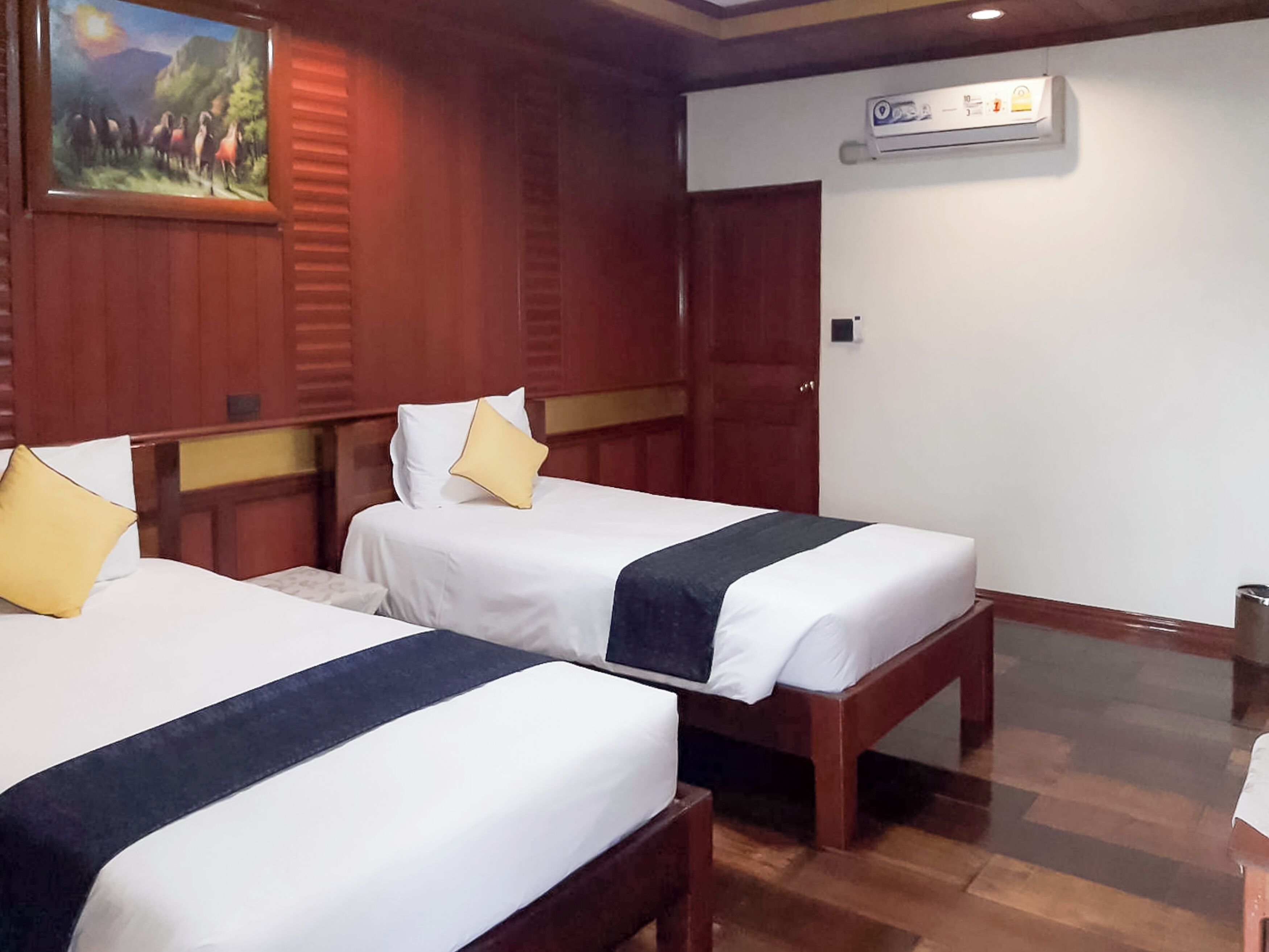 Une chambre d’hôtel avec deux lits, des têtes de lit en bois, du linge de lit blanc et un tableau au mur.