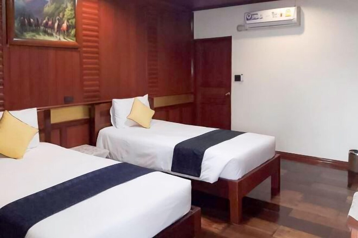 Une chambre d’hôtel avec deux lits, des têtes de lit en bois, un tableau au mur et un appareil de climatisation.