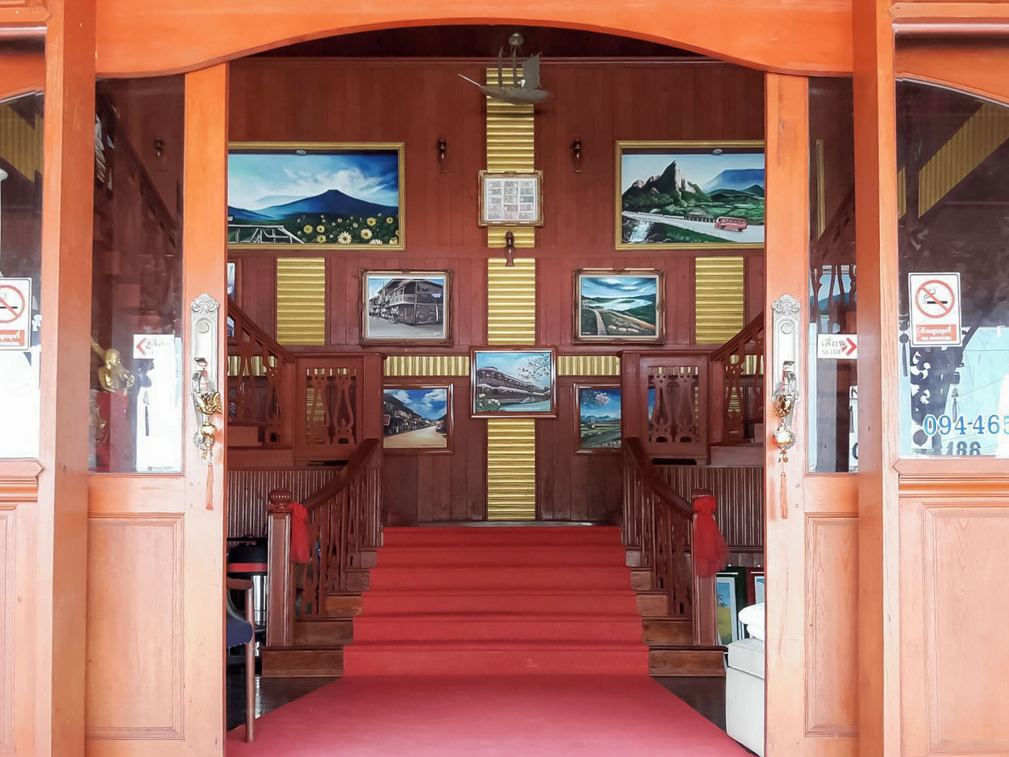 A wooden staircase with red carpet leading up to a door, flanked by framed pictures and a sign.