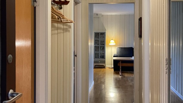 Un pasillo con suelo de madera, un perchero, un armario con puertas de cristal y un banco con lámpara.