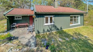 Una casa pequeña con techo de tejas rojas, un patio de piedra y fachada verde.