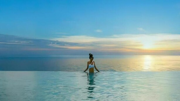 A person standing in a body of water with a sunset in the background. - Apec Mandala Resort - Mui Ne (Mui Ne)