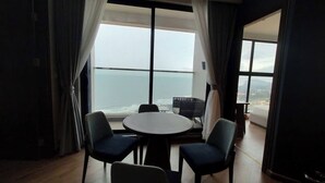 A room with a round table and four chairs, large windows with curtains, and a view of the sea. - Apec Mandala Resort - Mui Ne (Mui Ne)