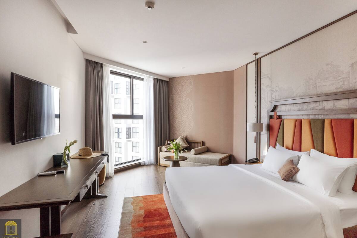 Ein Hotelzimmer mit einem großen Bett, einem Schreibtisch, einem Fernseher und einem Fenster mit Vorhängen.