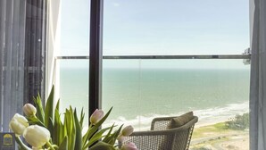 A balcony with a view of the ocean, a wicker chair, and a vase of tulips. - Apec Mandala Resort - Mui Ne (Mui Ne)