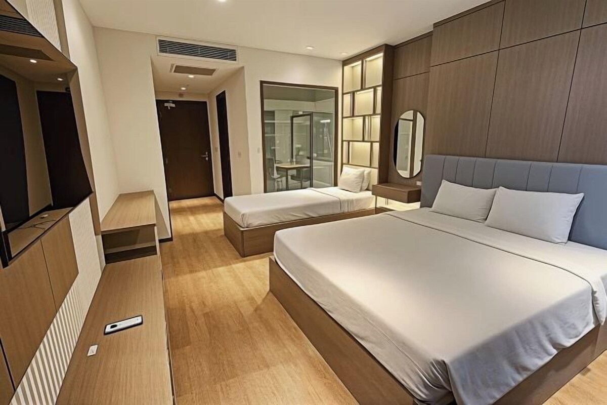 A modern hotel room with a large bed, a bedside table, a mirror, and a TV.