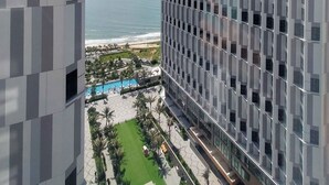 A modern hotel with a view of the ocean, featuring a pool area and a well-maintained lawn. - Apec Mandala Resort - Mui Ne (Mui Ne)