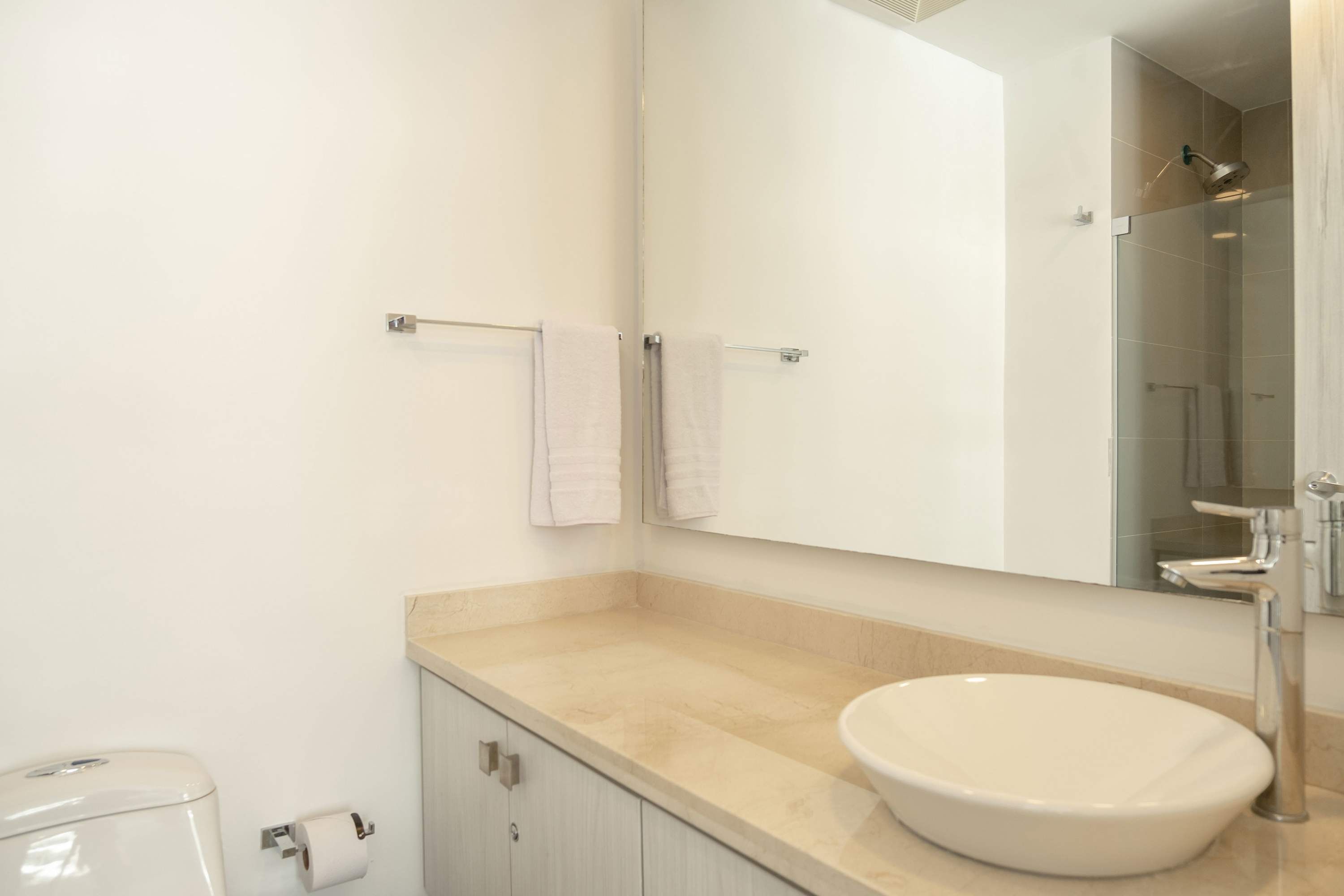 Un baño moderno con encimera color beige, un lavabo blanco y un espejo grande.