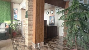 A reception area with a wooden reception desk, a green artificial grass wall, a clock, and a poster on the wall. - The Unmad Satovari (Dharamshala)