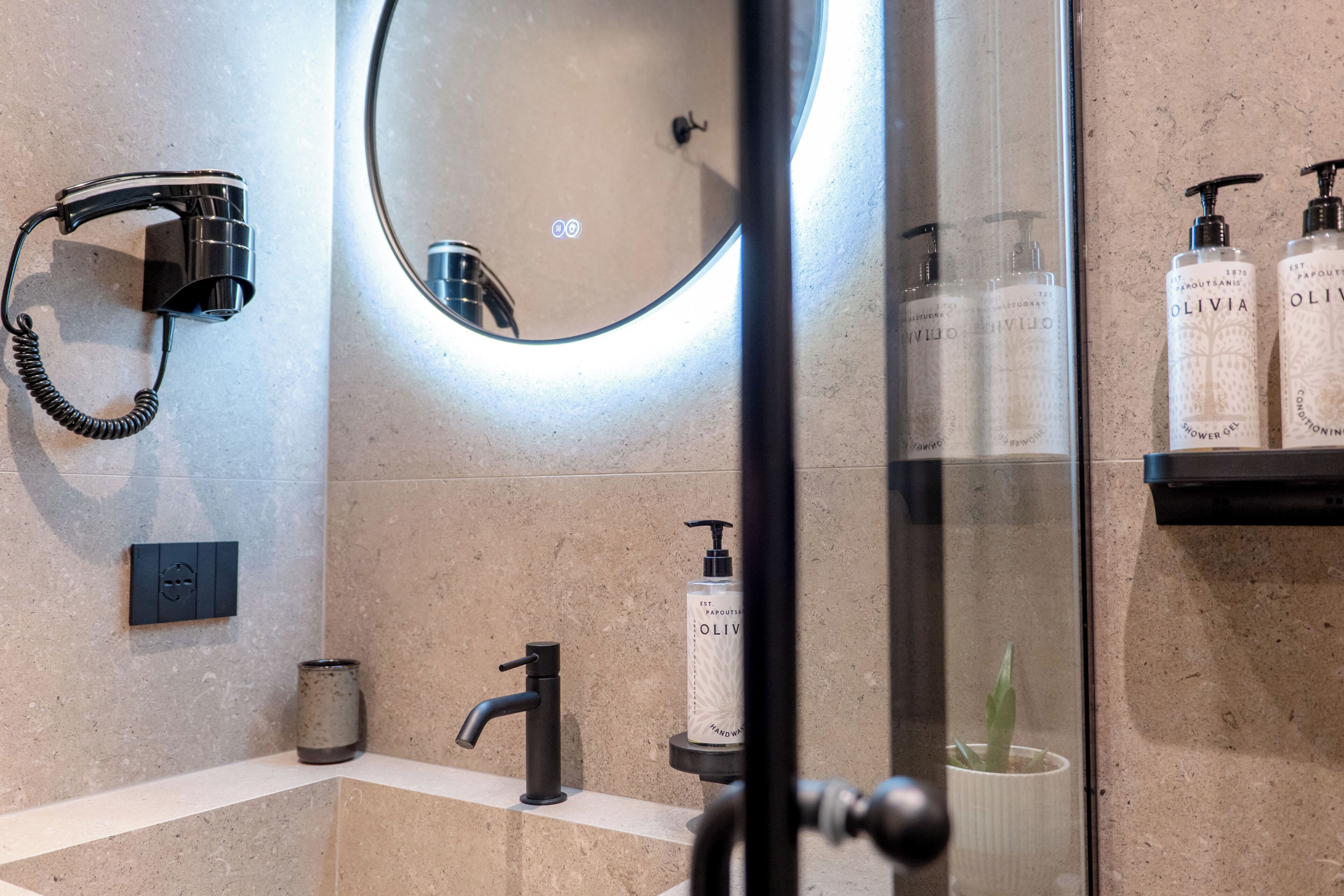 A bathroom with a hairdryer, a mirror, a sink, a faucet, and toiletries on a shelf.