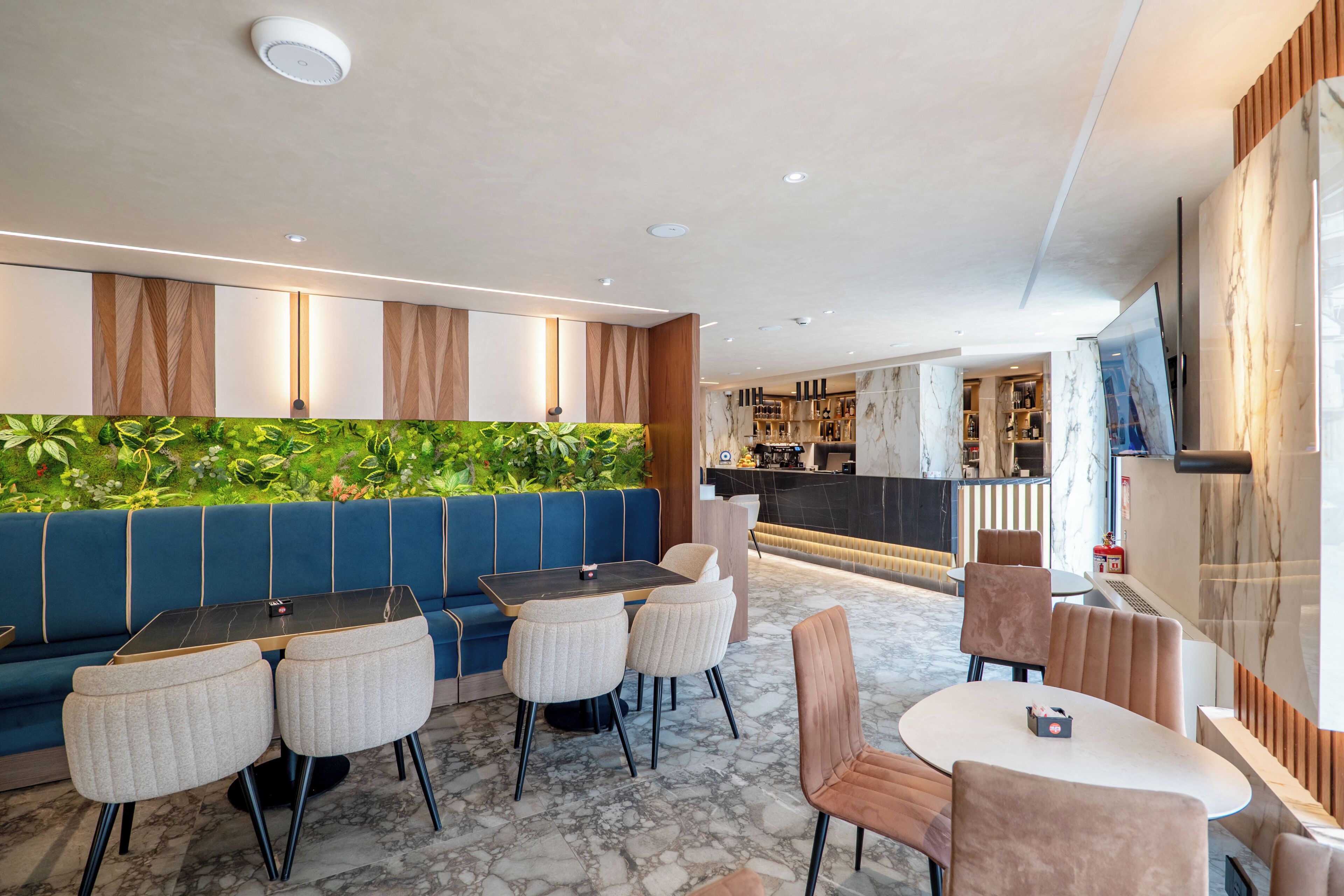 En moderne restaurant med blå bænke, marmorgulv og en bar i baggrunden.