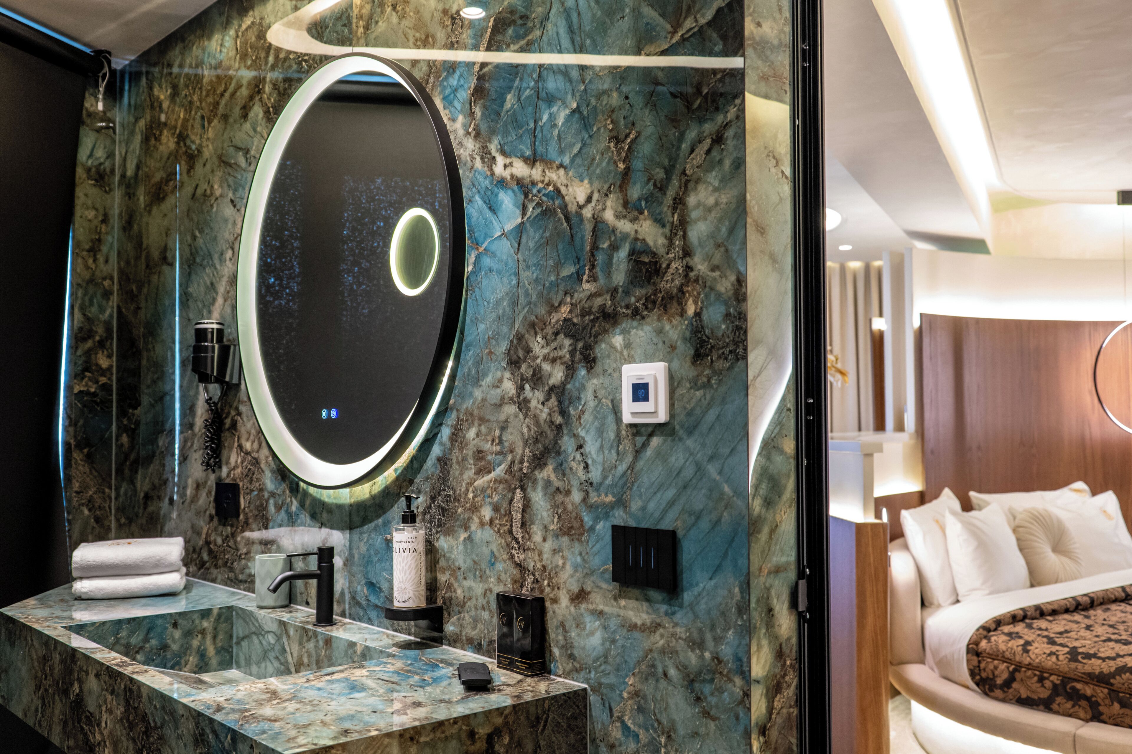 A bathroom with a marble wall, a round mirror, a sink, and a toilet.