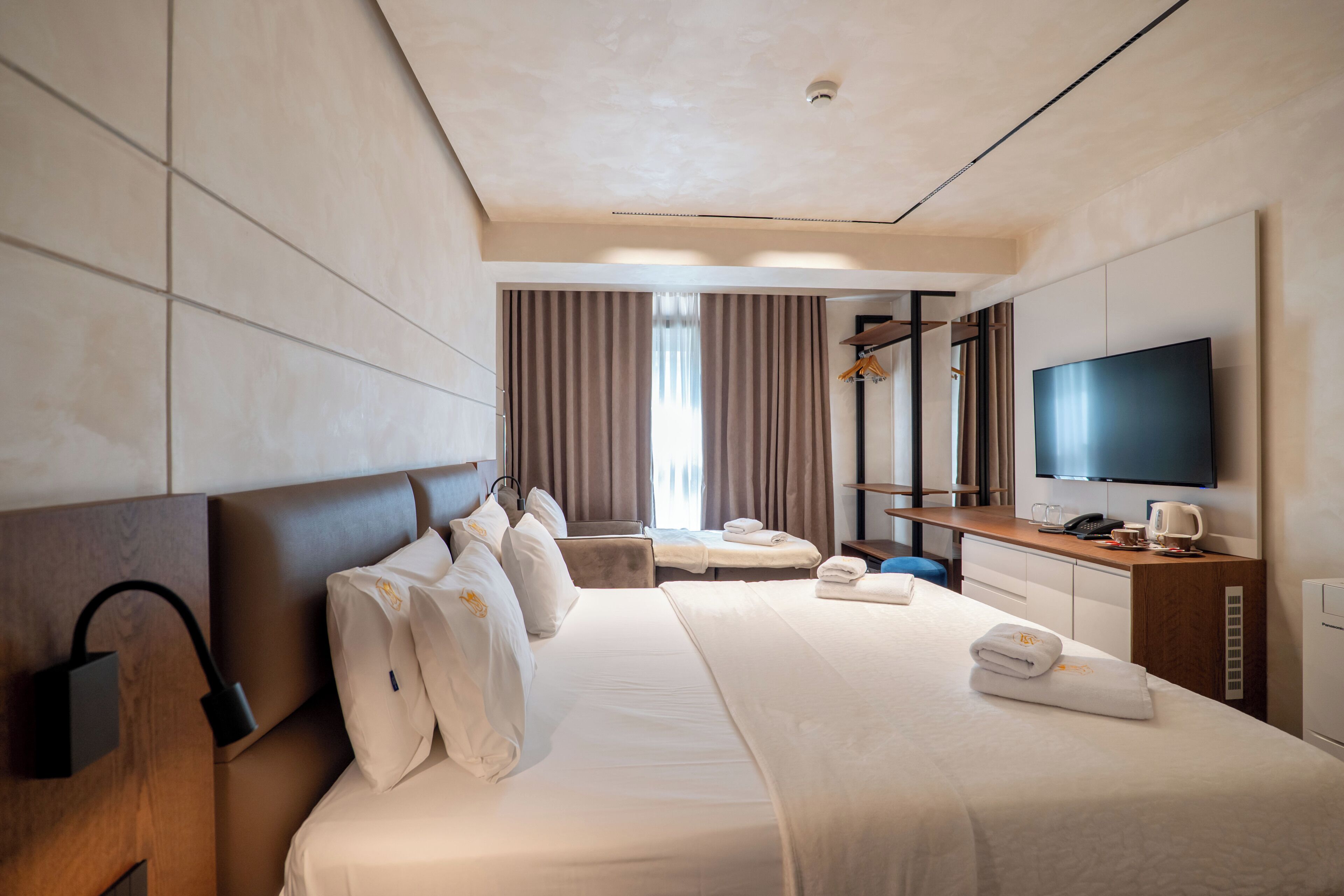 Ein Hotelzimmer mit einem großen Bett, einem Fernseher, einem Schreibtisch mit Stuhl und einem Fenster mit Vorhängen.