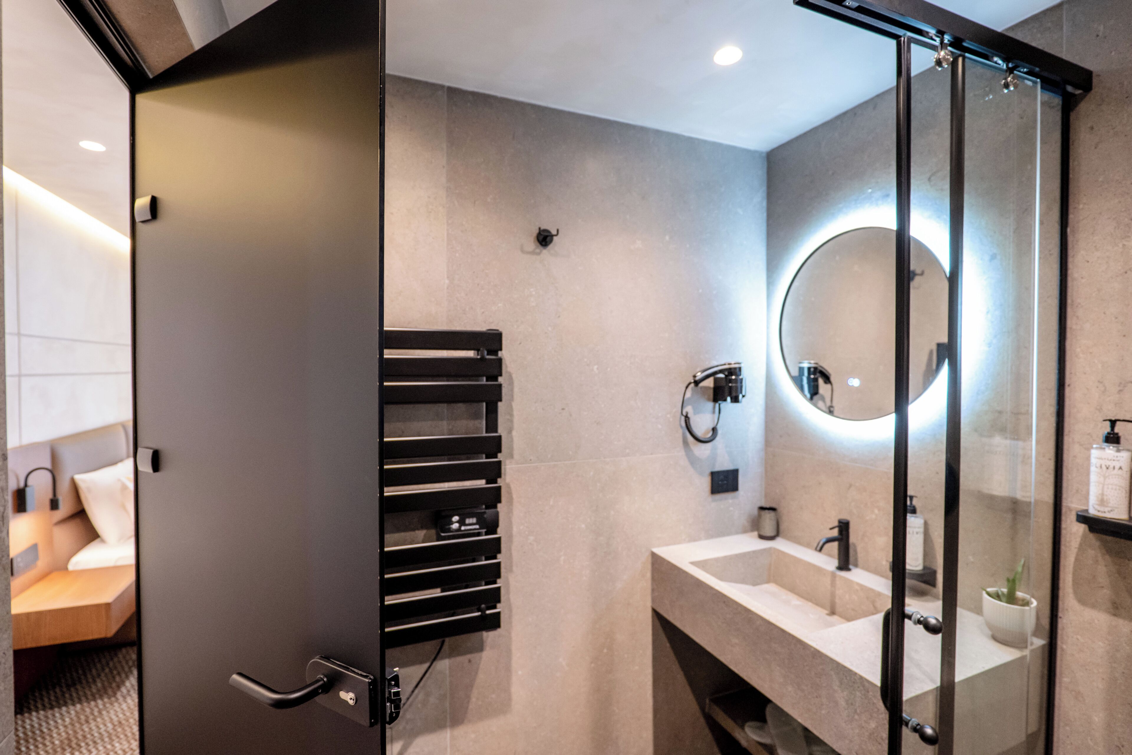 A modern bathroom with a glass shower enclosure, a round mirror, and a built-in towel rack.