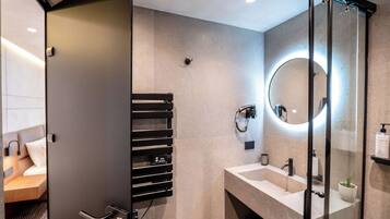 A modern bathroom with a glass shower enclosure, a round mirror, and a built-in towel rack.