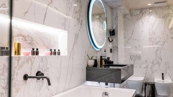Un baño moderno con pared de mármol, una bañera independiente, un tocador con espejo y un inodoro.
