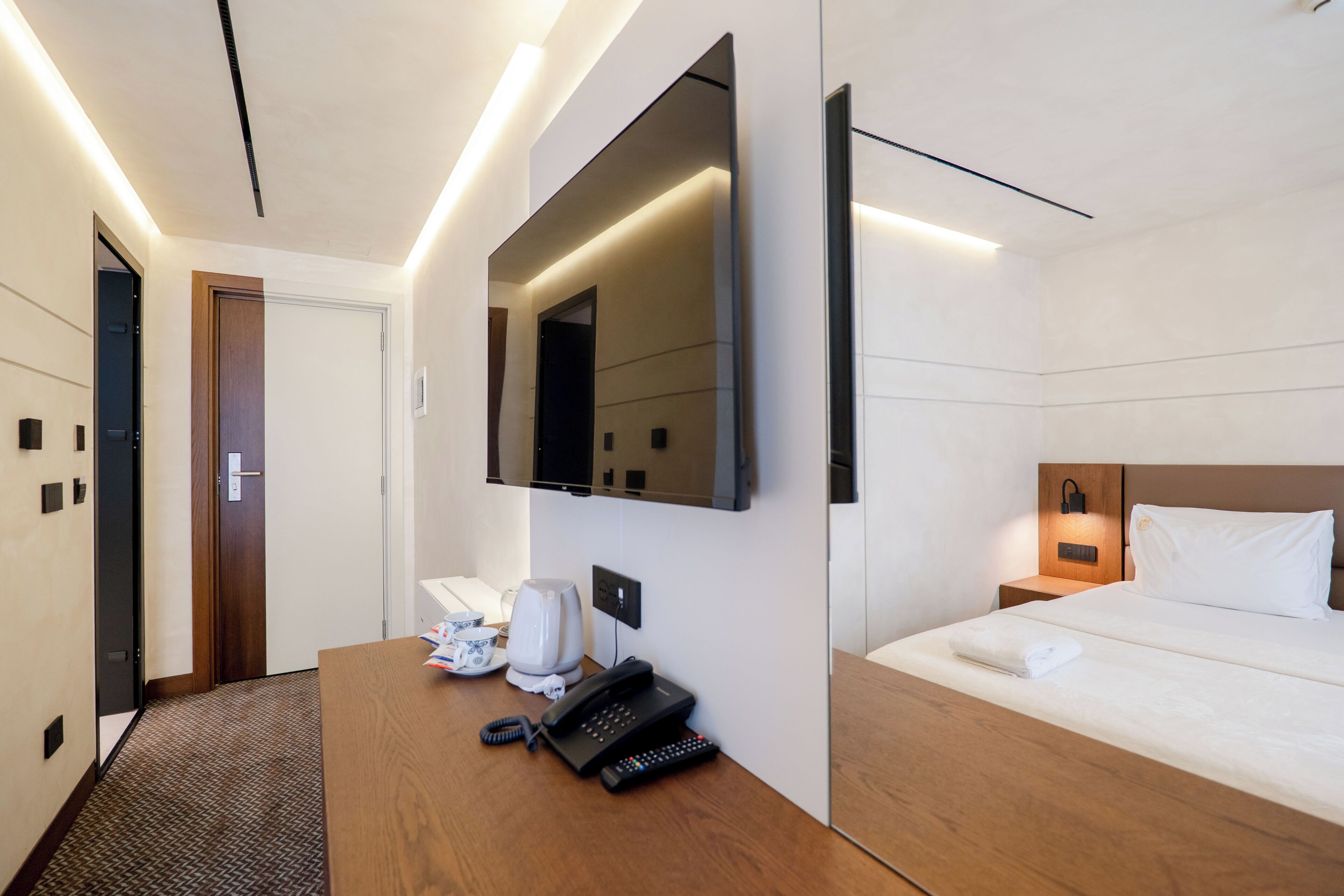 Ein Hotelzimmer mit Bett, Nachttisch, Spiegel, Fernseher, Telefon und einer Kaffeemaschine.