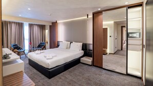 A modern hotel room with a large bed, a desk, a chair, a mirror, and a wardrobe. - Mattis Hotel (Tirana)