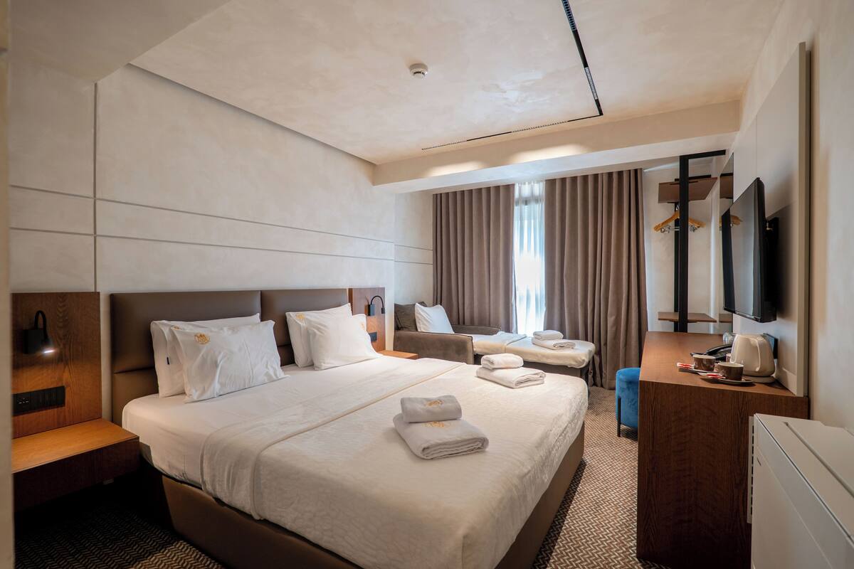 A hotel room with a large bed, a desk, a chair, a TV, and a mirror.