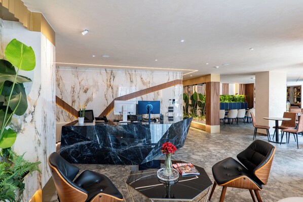 A modern hotel lobby with a marble reception desk, seating area, and indoor plants. - Mattis Hotel (Tirana)