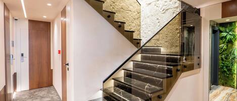 A modern staircase with glass railings and marble steps, leading to a room with a green wall mural.