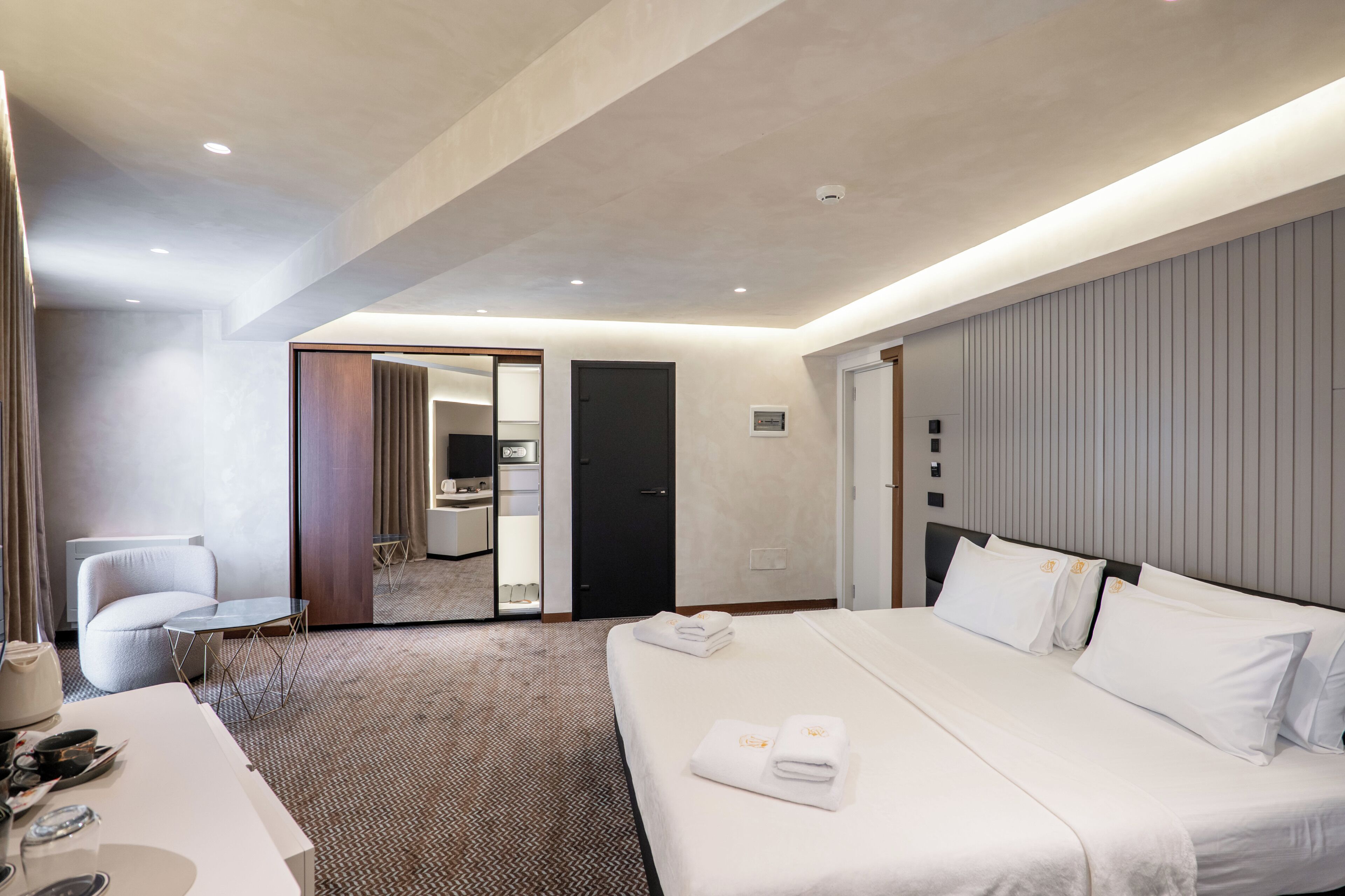 A hotel room with a bed, a desk, a chair, a mirror, and a door leading to a bathroom.