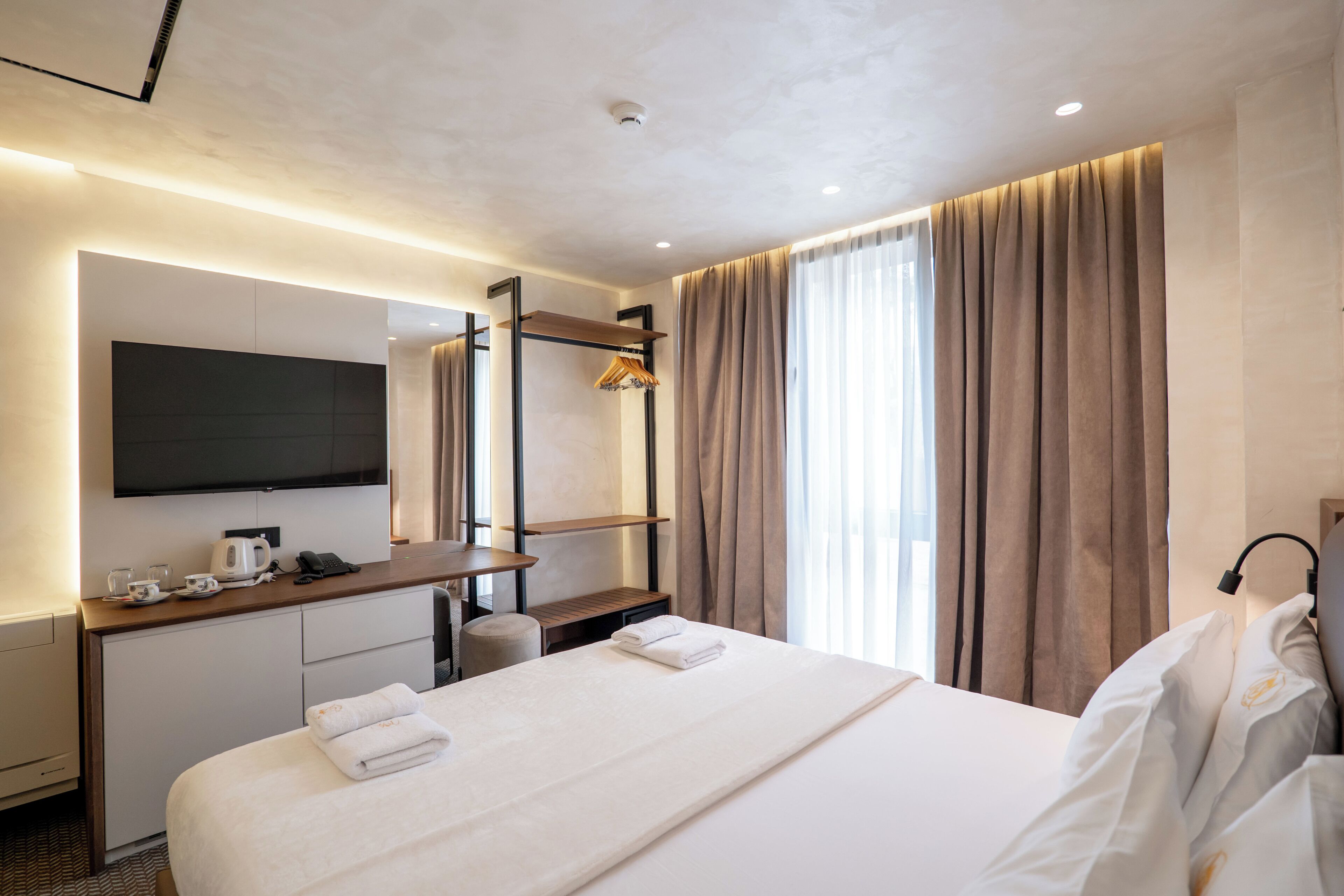 A hotel room with a bed, a desk with a flat-screen TV, a coffee maker, and a window with curtains.