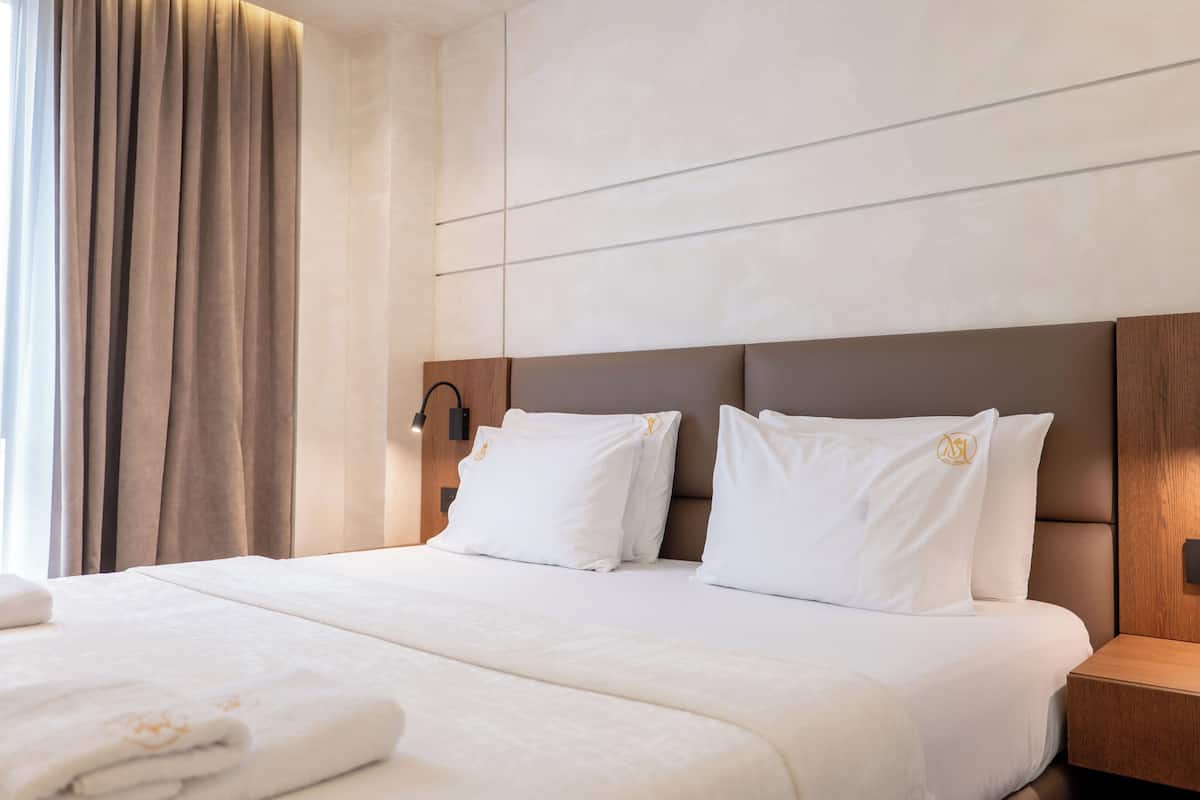 A neatly made bed with white linens, a wooden headboard, and a nightstand with a lamp.