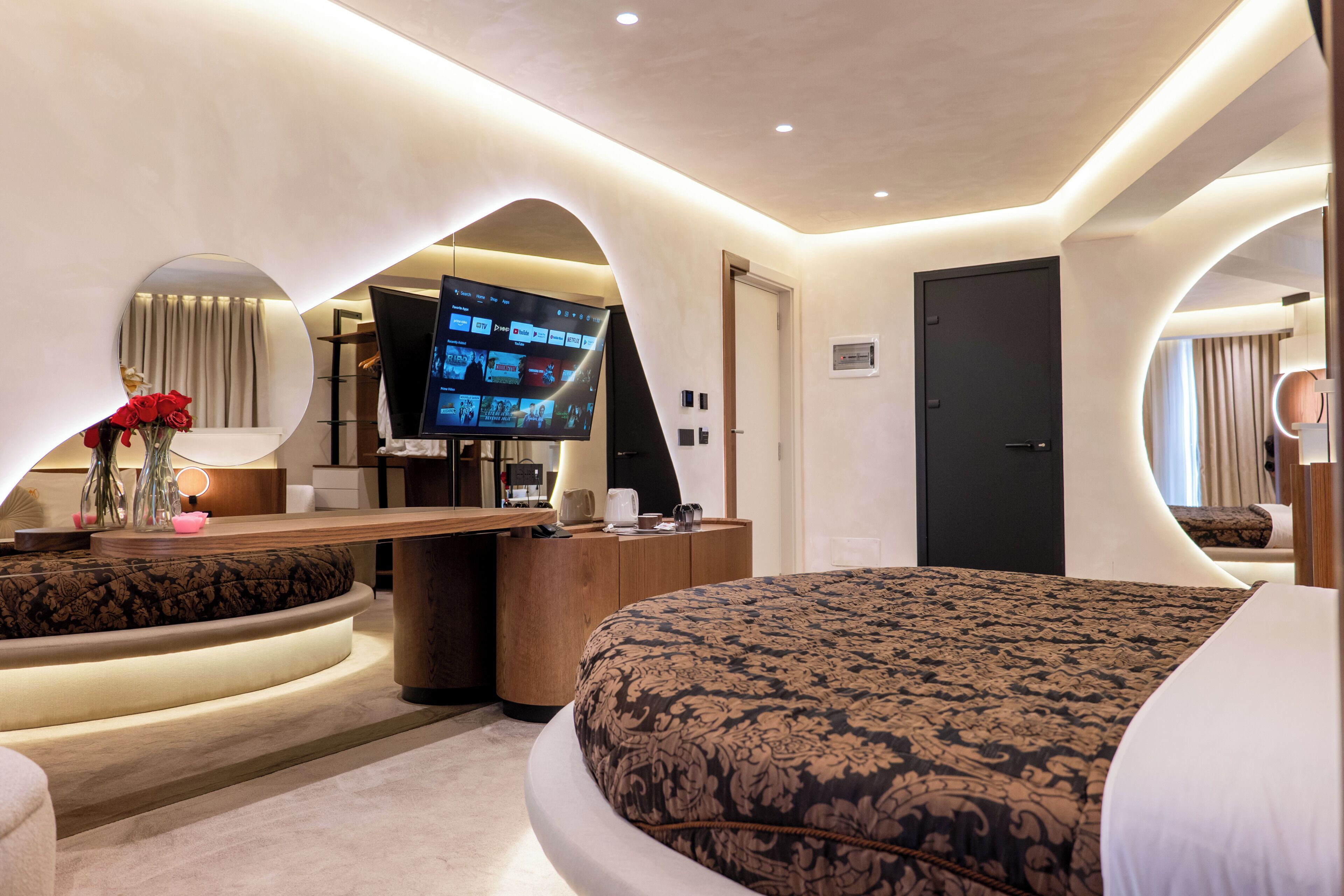 Una habitación de hotel moderna con una cama curvada, televisión, escritorio y espejo.