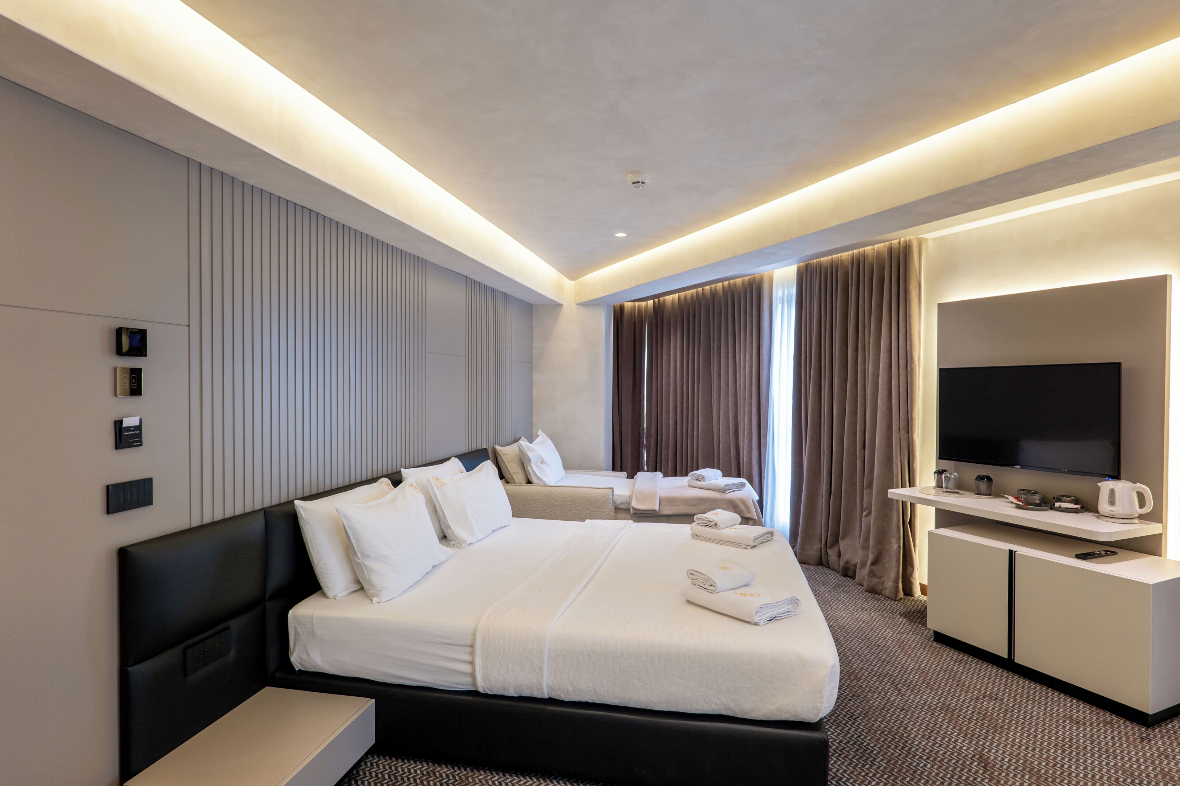 A hotel room with a large bed, a flat-screen TV, a desk with a coffee maker, and a seating area with a sofa and armchairs.