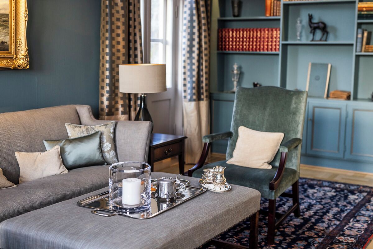 Un salon chaleureux avec un canapé gris, un fauteuil vert et un plateau sur lequel se trouvent une bougie et des couverts en argent.