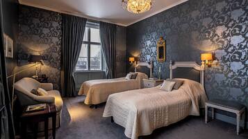 A hotel room with two beds, a chandelier, a window with curtains, and a mirror on the wall.