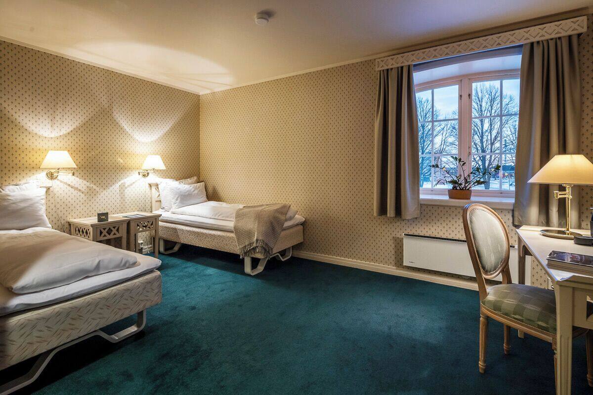 A hotel room with two beds, a desk, a chair, and a window with curtains.