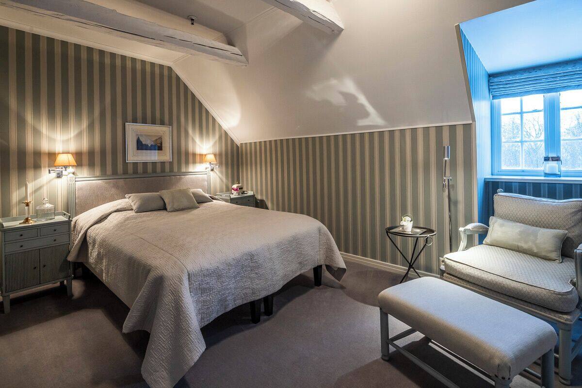 A bedroom with a bed, bedside lamps, a chair, and a window.