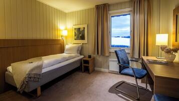 Ein Hotelzimmer mit Bett, Schreibtisch, Stuhl, einem Fenster mit Vorhängen und einer Lampe.