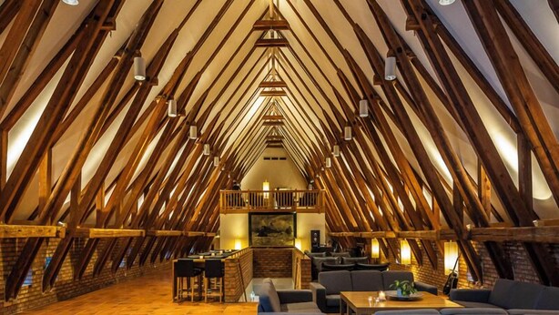 Habitación en el ático con techo inclinado, vigas de madera y zona de estar con sofás y una mesa.