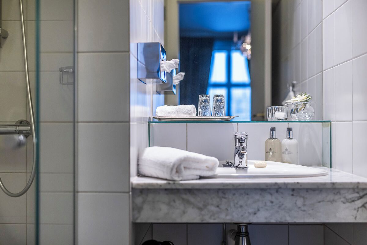 Un baño moderno con cabina de ducha de vidrio, un lavamanos de mármol y un estante de vidrio con artículos de aseo.
