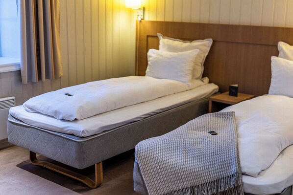 Habitación de hotel con dos camas individuales, una mesita de noche y un ventanal con cortinas.