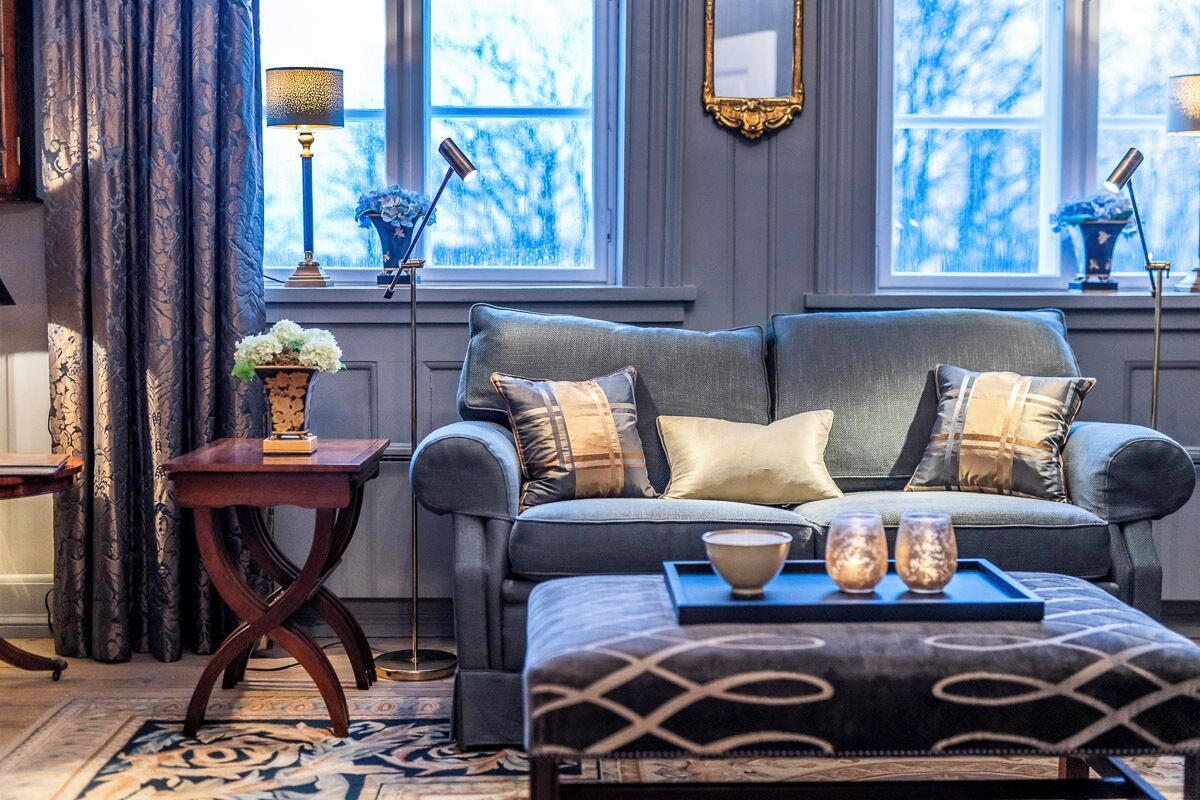 Un salon chaleureux avec un canapé gris, un pouf à motifs et un plateau avec des verres.