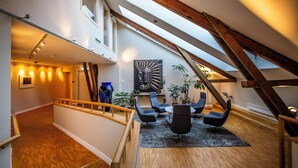 Amplio espacio tipo loft con techo alto, vigas de madera, tragaluces y un área de descanso con sillas modernas.