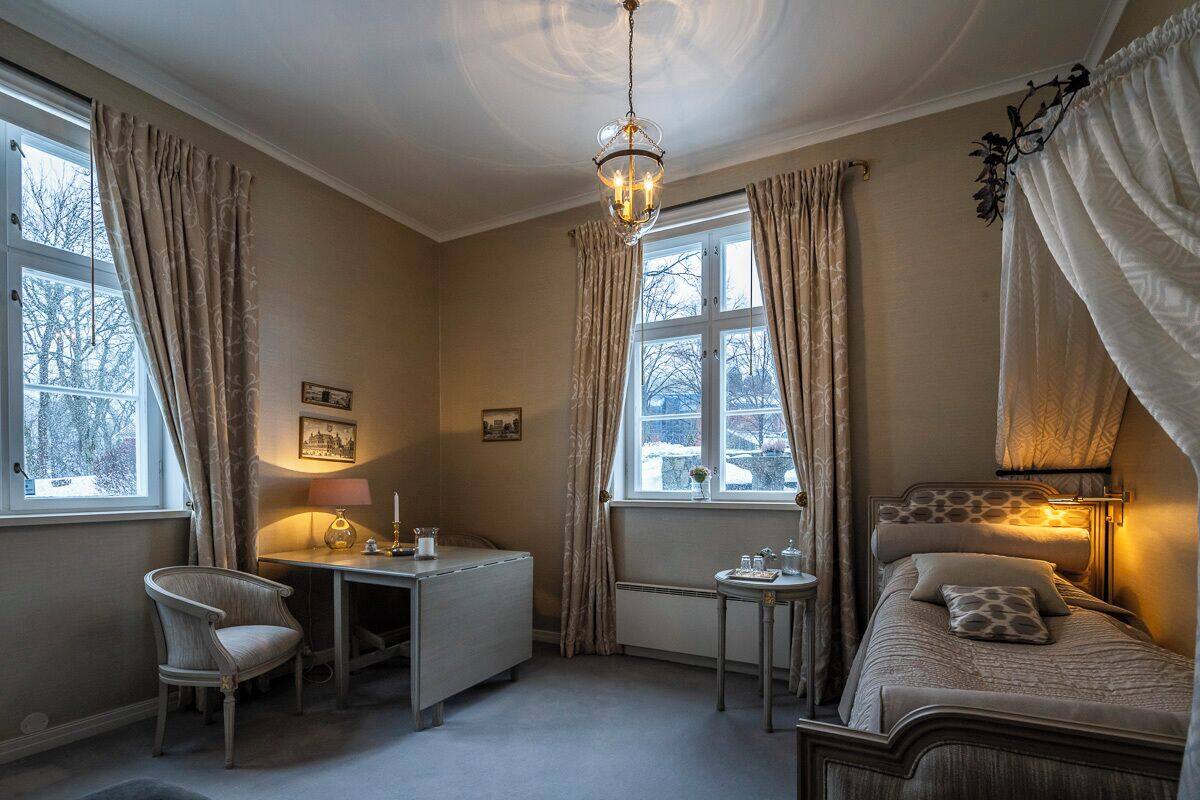 A bedroom with a desk, chair, and bed, featuring large windows and a chandelier.