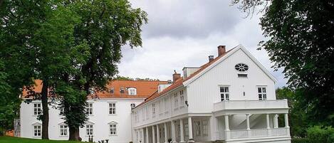 Un edificio blanco grande con una sección central y dos alas, rodeado de frondosos árboles verdes.