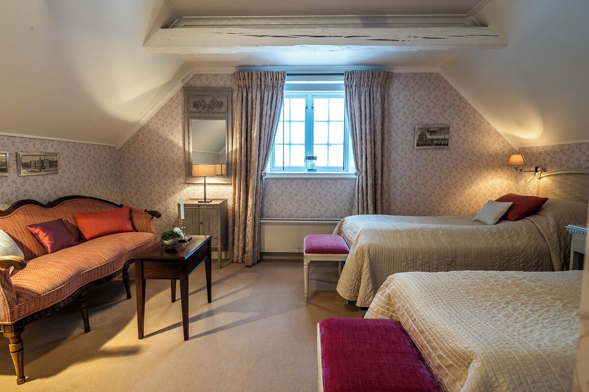 A cozy room with a sofa, two beds, a small table, and a window with curtains.