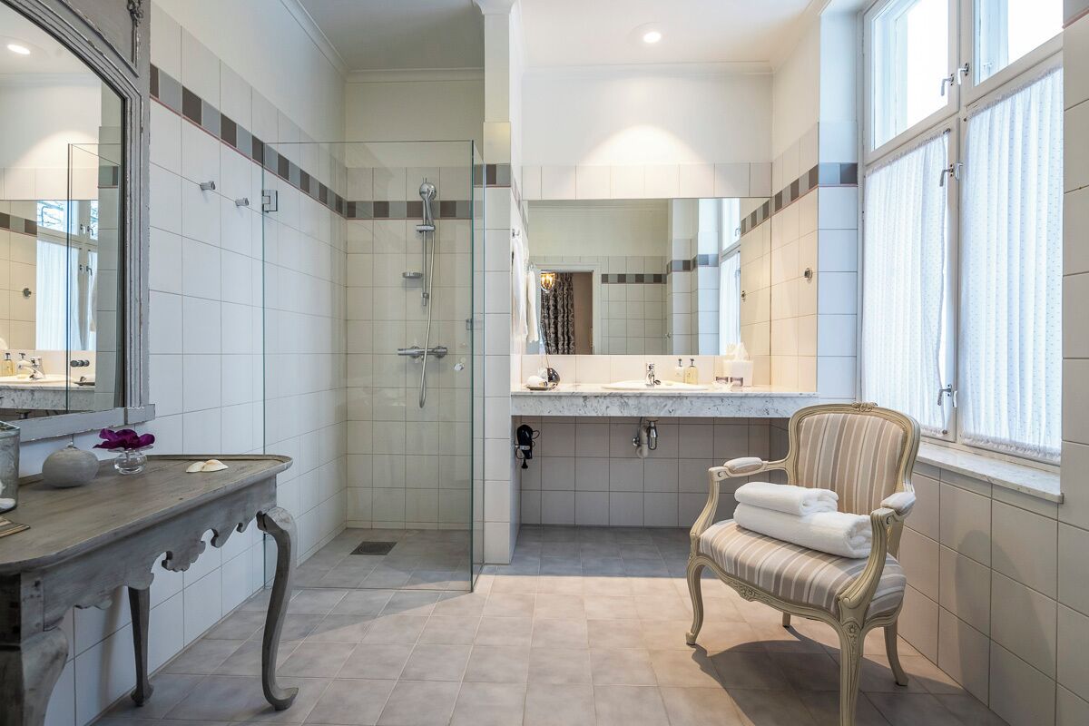 Un baño espacioso con cabina de ducha acristalada, tocador con espejo grande y una silla con toallas.