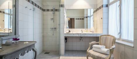 Un baño espacioso con cabina de ducha acristalada, tocador con espejo grande y una silla con toallas.