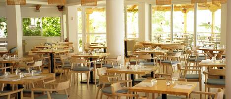 Un restaurant espaiós amb moltes taules i caires, finestres grans i llums de sostre de vímet.