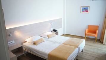 Quarto de hotel com duas camas, uma mesinha de cabeceira, uma cadeira laranja e um quadro na parede.