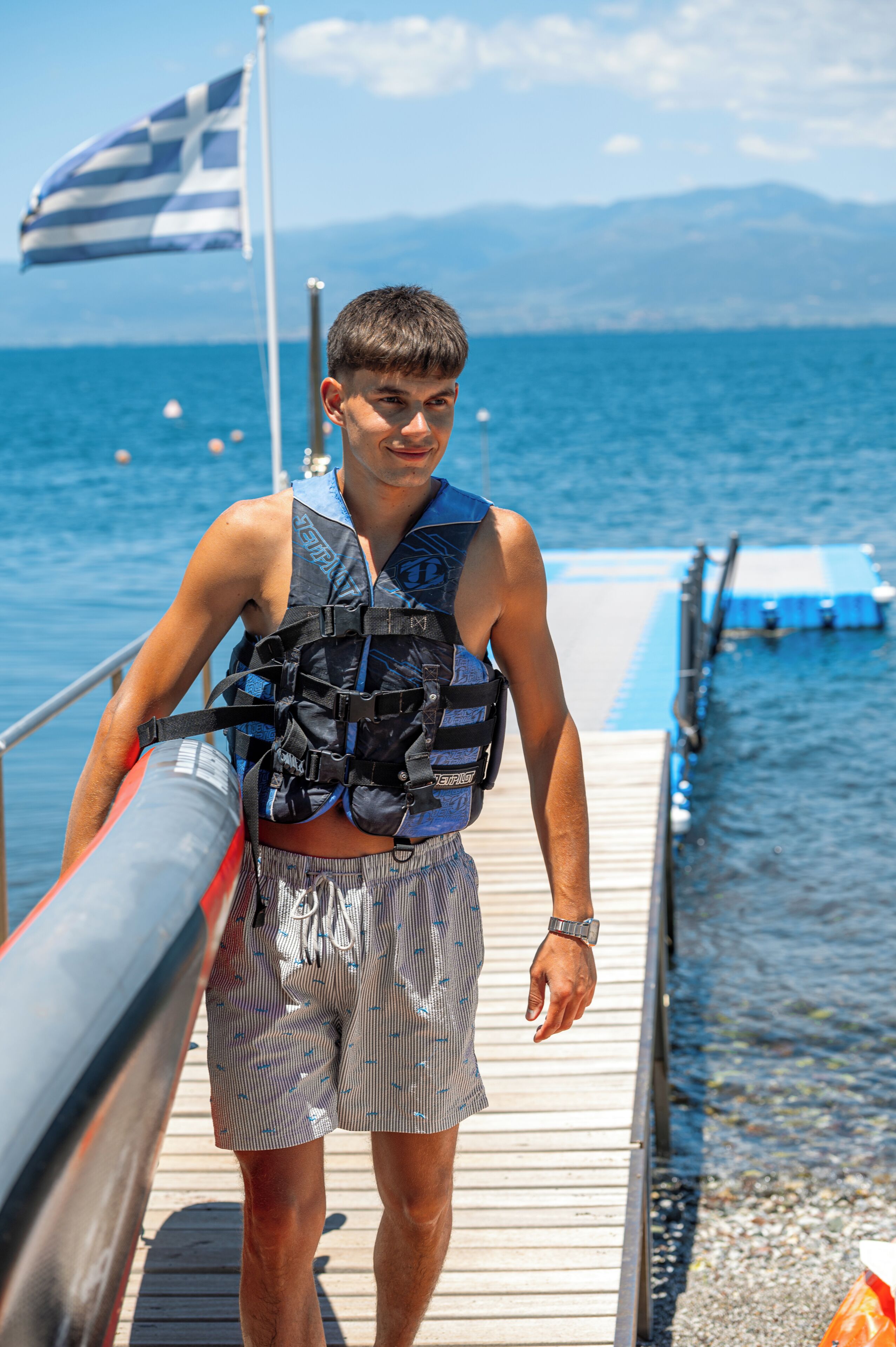 A person on a wooden dock with a body of water and a flag in the background.